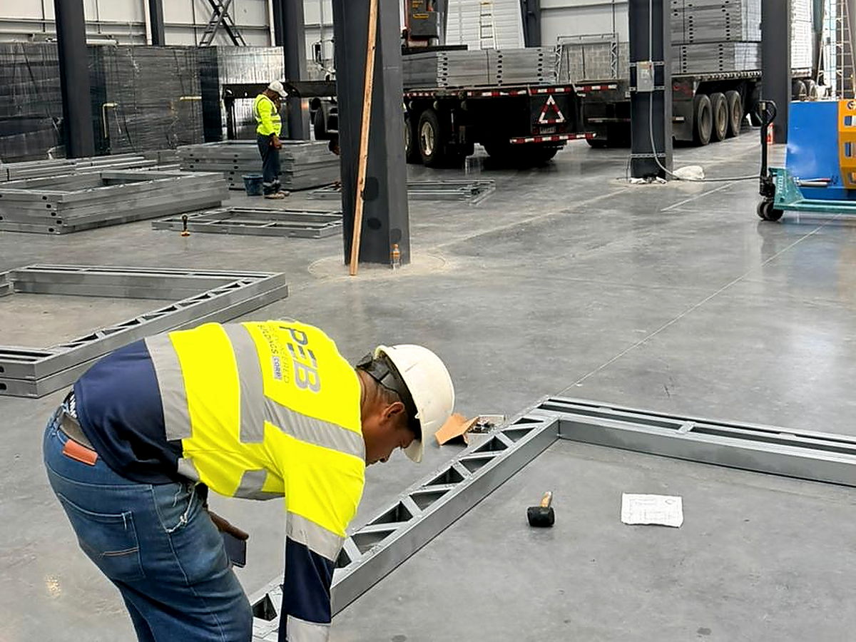 Operario verifica el armado y las escuadras de un marco estructural de acero conformado en frío contra el plano de taller, en la planta del grupo operada por NewCon Steel® en Las Mañanitas